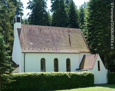 Außenansicht der Kapelle Maria im Elend umrahmt von Bäumen mit davor liegender Hecke.