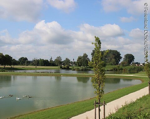 Blick auf den Landschaftssee im Schmuttergrün mit um den See verlaufenden Wegen.