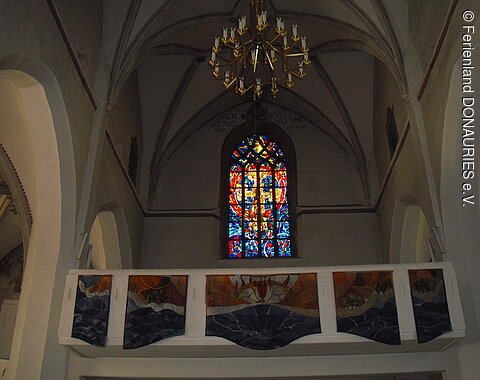 Blick auf die schlichte Empore mit dahinter liegendem Buntglasfenster