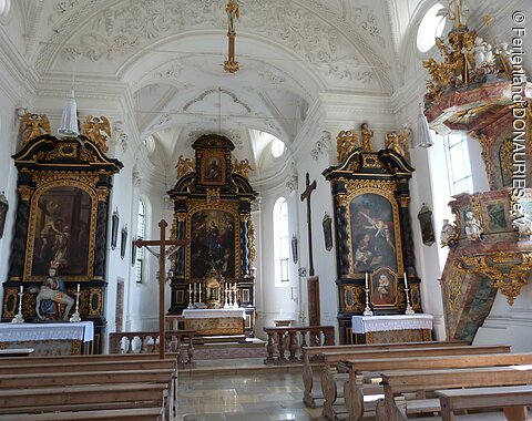 Blick in die helle, lichtdurchflutete Schlosskirche. Vorne in der Mitte der Hauptaltar, links und rechts die Seitenaltäre sowie ganz rechts im Bild die Kanzel.