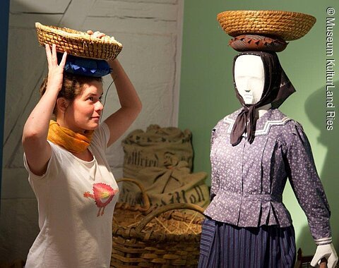 Eine Frau führt vor, wie die Körbchen früher auf dem Kopf getragen wurden