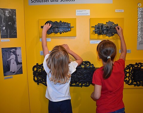Schlüssel & Schloss Zwei Kinder probieren alte, an der Wand befestigte Schlösser aus