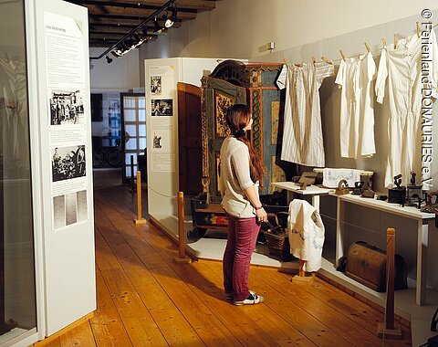 Eine Frau betrachtet aufgehängte alte Wäschestücke im Heimatmuseum in Rain