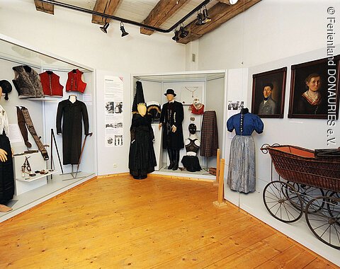 Verschiedene ausgestellte Trachten und ein alter Kinderwagen im Heimatmuseum in Rain