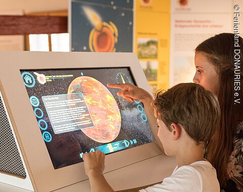 Zwei Kinder schauen sich die Infomationen auf dem Infoterminal im Geopark Infozentrum in Nördlingen an