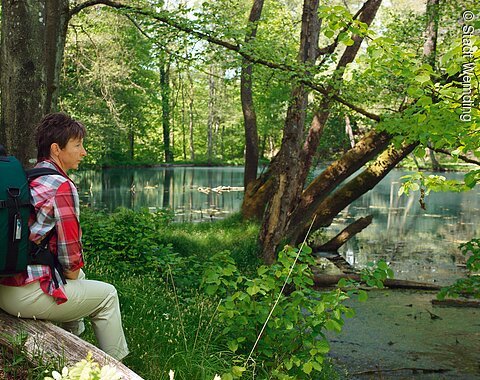 Eine Wanderin sitzt am idyllischen Doosweiher und blickt auf das Wasser.