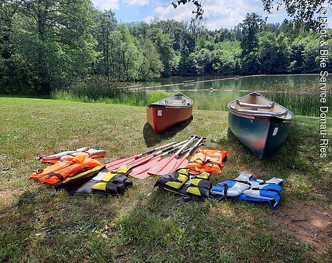 Zwei Kanus an einer Anlegestelle an der Wörnitz. Davor befinden sich Schwimmwesten und Paddel.