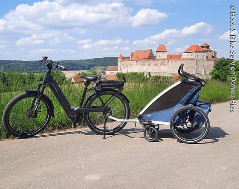 E-Bike mit Fahrradanhänger für Kinder auf einem Radweg bei Harburg. Im Hintergrund ist das Schloss Harburg zu sehen.