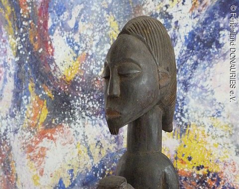 Sonderausstellung AFRIKA im Kunstmuseum Wemding Eine afrikanische Figur aus Holz. Dahinter ein buntes Gemälde.
