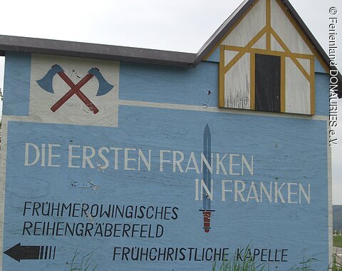 Ein großer hölzerner Wegweise zur rekonstruierten frühchristlichen Kapelle