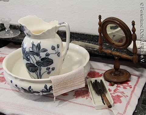 Ein Waschtisch mit weiß-blauer Waschschüssel, weiß-blauem Waschkrug und kleinem Spiegel