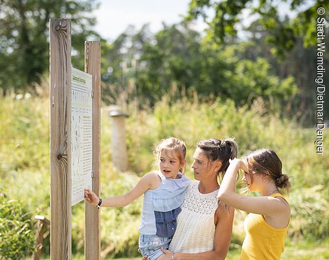 Familie im Obstlehrgarten Eine Familie betrachtet eine Informationstafel im botanischen Obstlehrgarten und schafft sich einen Überblick.