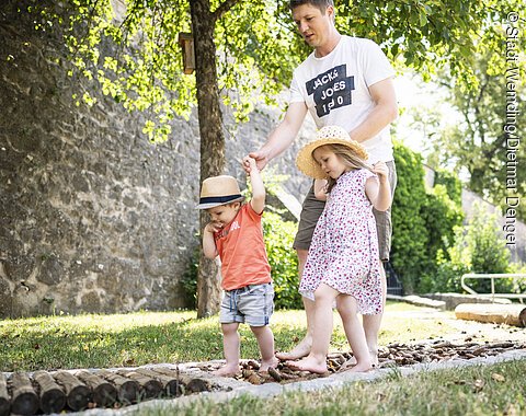 Ein Vater läuft mit seinen zwei Kinder auf dem Barfußpfad im Stadtgraben.