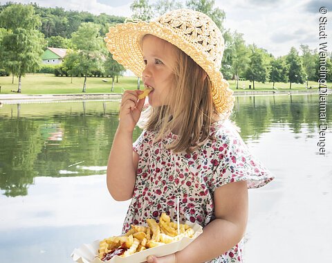 Mädchen isst Pommes auf der Seeterrasse am Waldsee.