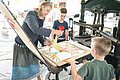 Die Leiterin des KunstMuseums führt zwei Jungs den Bilddruck mit einer alten Maschine vor.