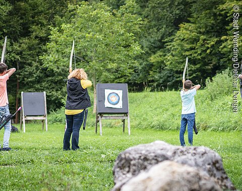Eine Familie steht mit Pfeil und Bogen auf einer Wiese.