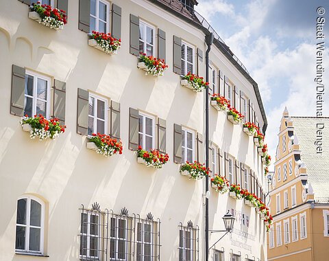 Das Verwaltungsgebäude von außen im Sommer mit Blumenkästen an den Fenstern.