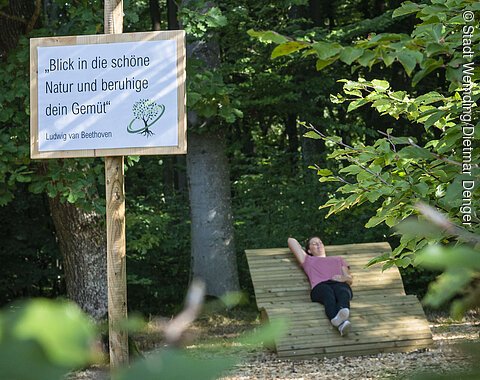 Eine Frau liegt auf einer Holzliege beim Waldbaden.