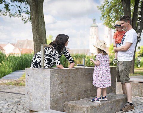 Eine Frau testet das Handkneippbecken am Johannisweiher. Der Mann und die beiden Kinder sehen ihr dabei zu.