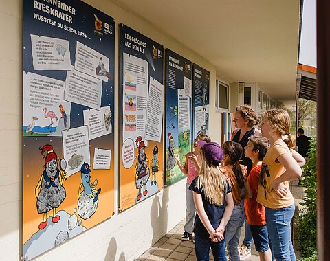 Eine Gruppe Kinder betrachtet Informationstafeln an einer Hauswand.
