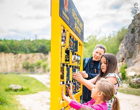 Eine Frau und drei Kinder spielen ein Outdoor-Memory.