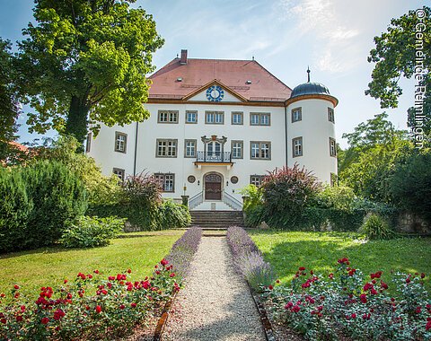 Blick auf das Schloss Reimlingen mit dem davor liegenden Park mit seinen Blumenbeeten und Bäumen.