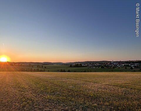 Sonnenuntergang über einem Feld. Am Bildrand ist der Markt Bissingen erkennbar