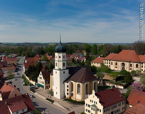 Inmitten der Wohnhäuser Wallersteins ragt der Turm der Pfarrkirche aus; Im Hintergrund die Hofreitschule