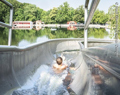 Ein Kind rutscht auf der Wasserrutsche am Waldsee herunter.