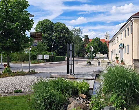 Ein teilweise begrünter Platz entlang der Hauptstraße und einem Gasthof an der Seite