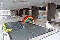 Innenansicht eines Schwimmbads, dem Jurabad Monheim, mit Kinderbecken, Regenbogenrutsche und Wasserspielzeugen. Im Hintergrund ein weiteres Schwimmbecken und ein großes offenes Fenster.