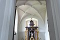Ein Blick durch eine Tür zu einem Kirchenaltar in der Walburgakapelle in Monheim, mit goldenen Verzierungen und einer Statue, der heiligen Walburga. Der Kirchenaltar ist umgeben von Kerzen und Blumen, in einem gewölbten Raum mit einer verzierten Decke.