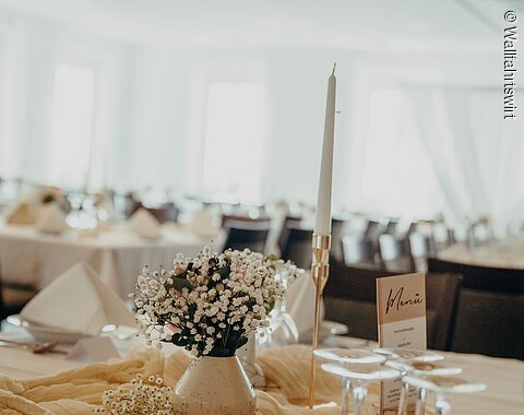 Blick auf einen in hellen Farben gedeckten Tisch mit Gläsern, Blumenvase und Kerze.