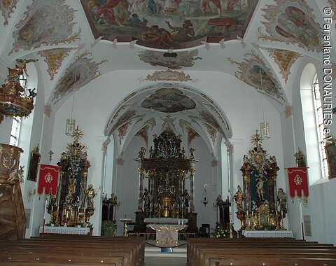 Blick in den hellen Innenraum mit Hauptaltar und den zwei Seitenaltären. Links zu sehen ist die Kanzel.