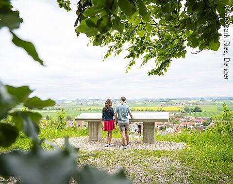 Ein Mann und eine Frau stehen am Aussichtspunkt des Geotops Kühstein mit Blick in das Kraterbecken.