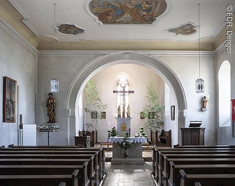Innenraum einer Kirche mit Bänken, Altar und bemalter Decke.