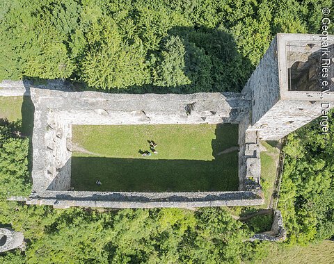 Luftaufnahme einer rechteckigen Burgruine mit einem Turm, umgeben von dichtem Wald.