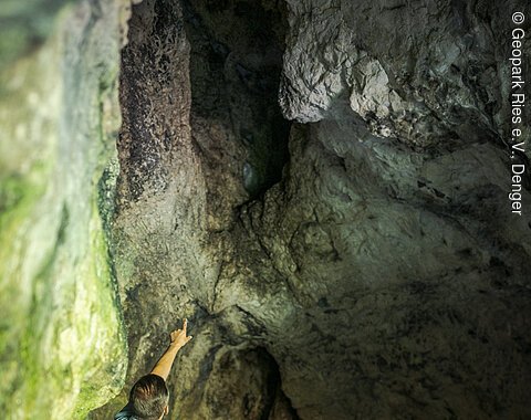 Eine Familie steht in einer Höhle, ein Erwachsener zeigt auf eine Felswand.