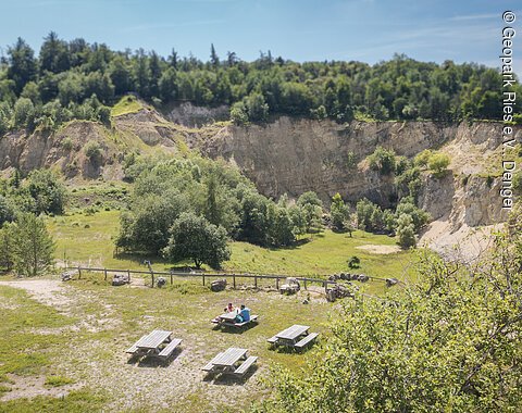 Eine Landschaft mit steilen Felswänden, Bäumen und mehreren Picknicktischen im Vordergrund.