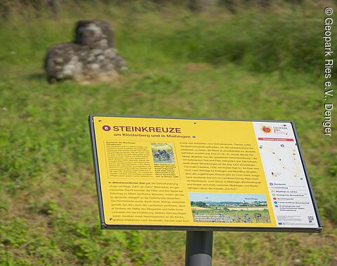 Informationsschild über Steinkreuze am Klosterberg und in Maihingen, im Hintergrund zwei Steinkreuze auf einer Wiese.