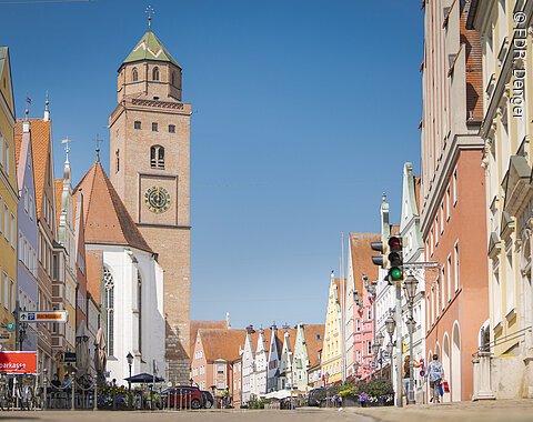Reichsstraße Donauwörth Straßenszene mit bunten Gebäuden und einem Kirchturm im Hintergrund, Ampel im Vordergrund.