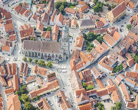 Luftaufnahme einer Stadt mit einer großen Kirche im Zentrum, umgeben von Gebäuden mit roten Dächern und Straßen.