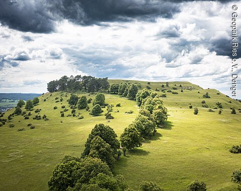 Der Ipf bei Bopfingen Hügelige Landschaft mit grünen Wiesen und Bäumen unter bewölktem Himmel.