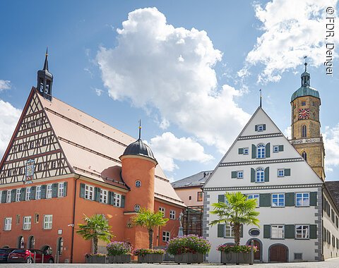 Alte Gebäude mit schönen Holzbalken, hinter denen ein Kirchturm zu sehen ist.