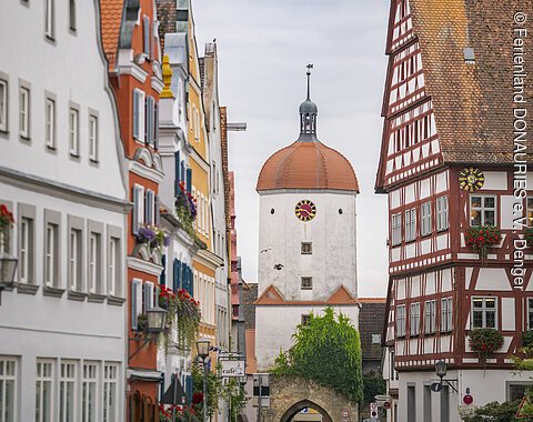 Straße mit historischen Gebäuden und einem Turm mit Uhr in der Mitte, umgeben von Fachwerkhäusern.