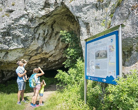 Familie an den Ofnethöhlen Eine Familie steht vor einer Höhle und betrachtet ein Informationsschild mit der Aufschrift "Ofnethöhlen".