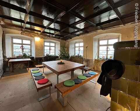 Amtsstube im Haupthaus, Wasserschloss Trochtelfingen Raum mit Holztisch, Sitzbänken mit bunten Kissen, vier Fenstern und Weihnachtsbaum in der Ecke.