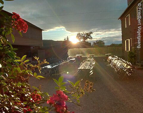 Innenhof Wasserschloss Trochtelfingen Blumen im Vordergrund, Tische und Stühle auf einem Hof, Sonnenuntergang hinter Gebäuden und Bäumen.