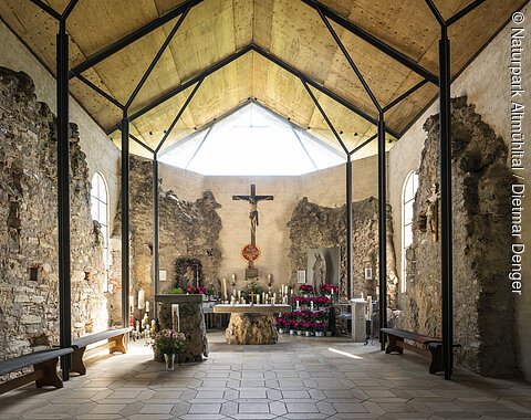 Ruinenkirche Spindeltal Innenraum einer Kapelle mit Altar, Kreuz, Kerzen und Blumen, umgeben von alten Steinmauern und Holzdecke