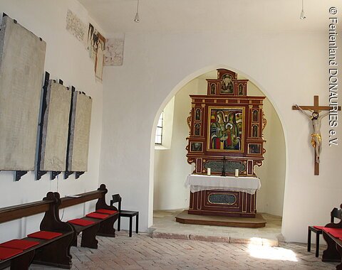 Blick in das schlichte Innere der Kapelle und auf den Altar mit dem Bild, das von dem verstorbenen Künstler Ernst Steinacker geschaffen wurde.